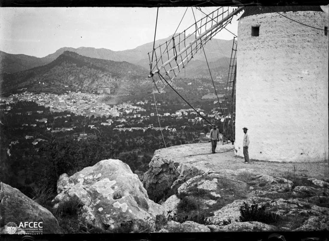 Dos homes al costat d'un molí de vent i al fons la ciutat de Palma de Mallorca