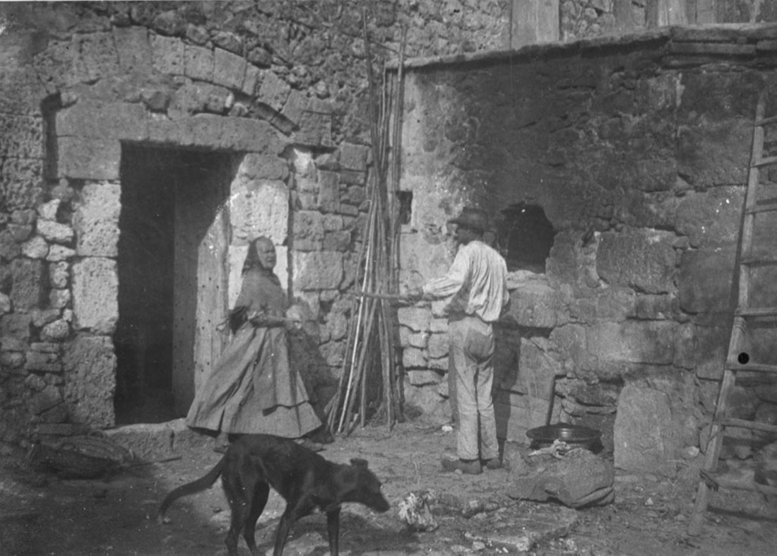 Pati de Capocorp Vell amb un home posant coses en un forn, una dona i un gos