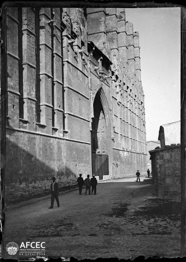 Façana lateral de la catedral de Palma de Mallorca amb un portal i homes passejant pel carrer